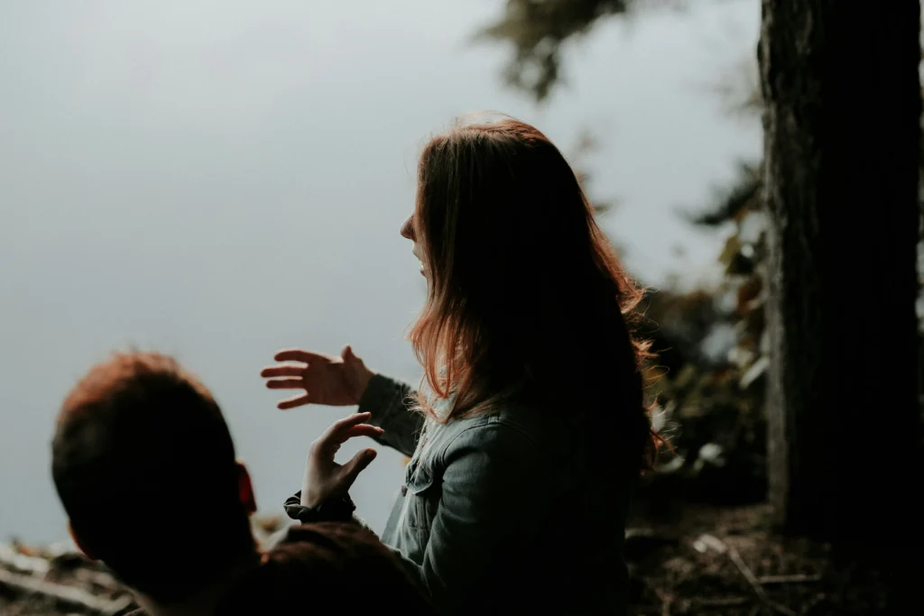 Two people in conversation at the edge of a wooded path